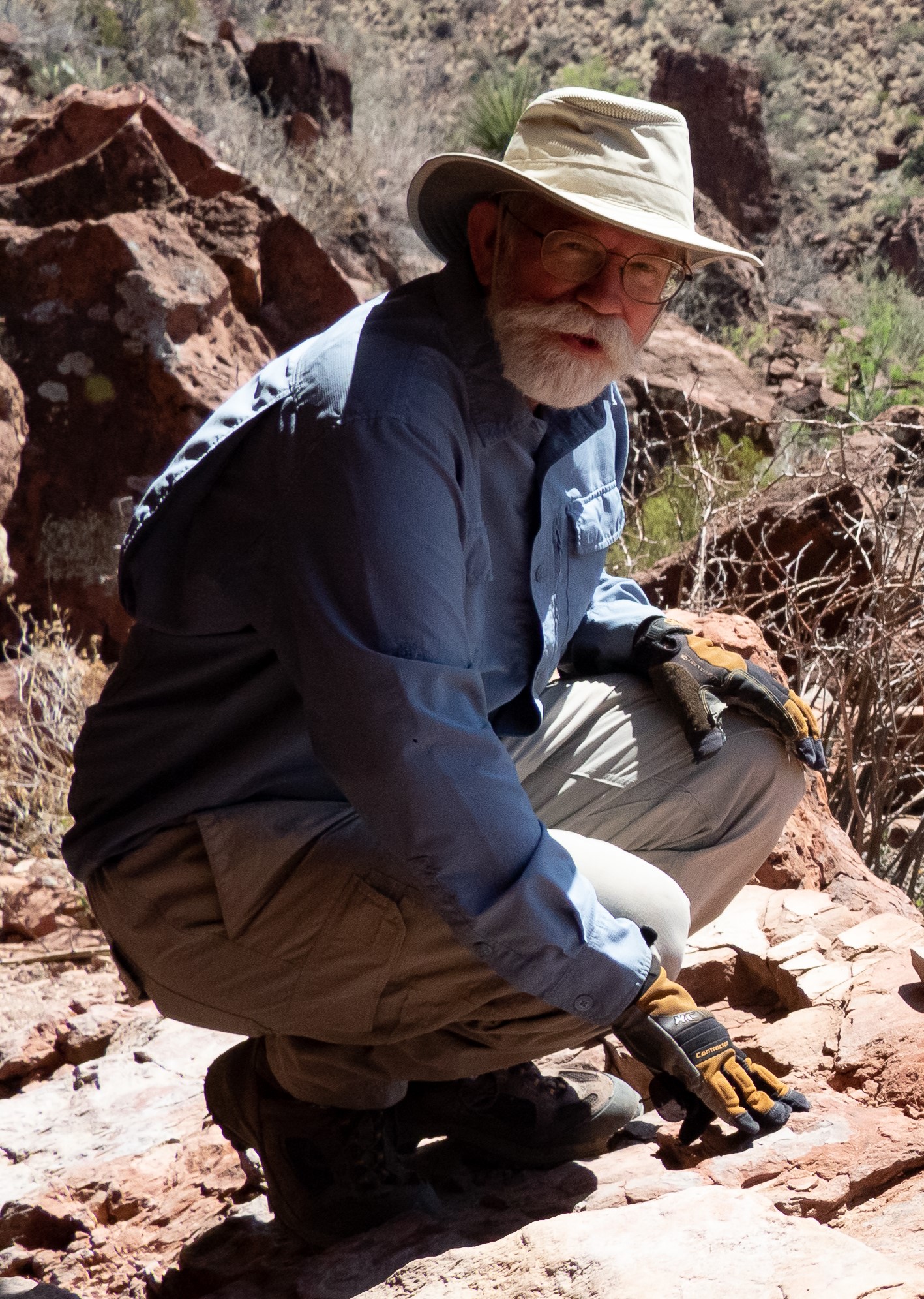 photograph of man squatting under a rock overhang