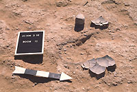 Broken ceramic bowl and grinding stone on floor of Room 11 around the as-yet unexcavated plastered hearth