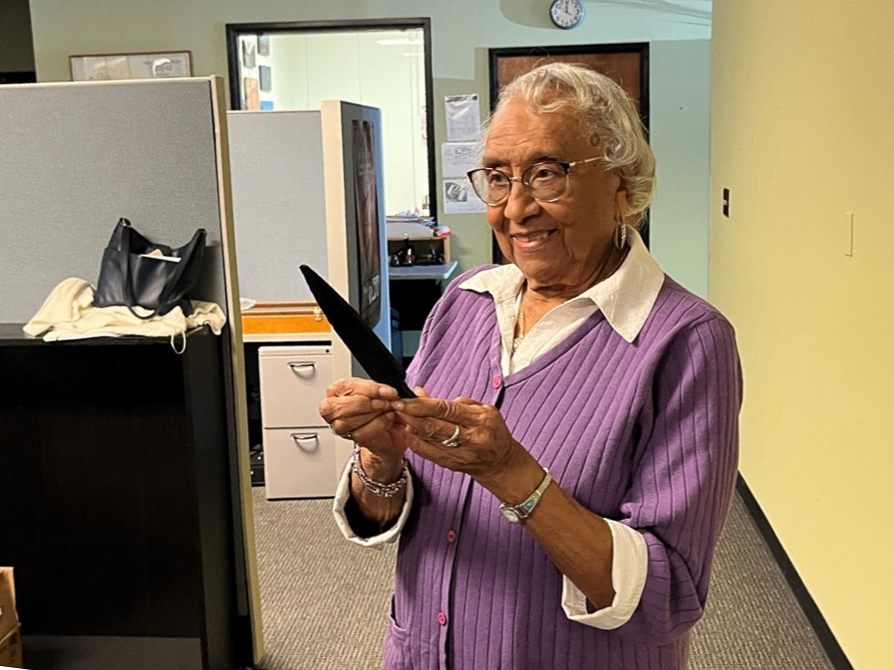 color photo of a woman standing in an office, smiling and holding a clinching bar