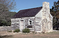 Side view of restored house, with chimney rebuilt. Wagon wheel hanging on chimney was found in adjacent field. Photo by Tom Hester.