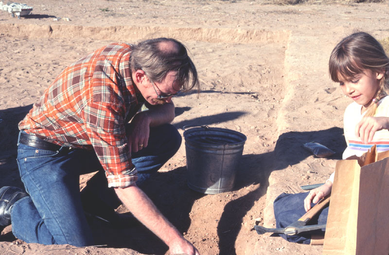 photograph of a man and a child digging in the desert