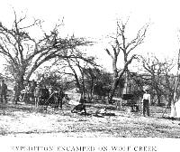 Old photo showing students, tent, and automobile in wooded area.