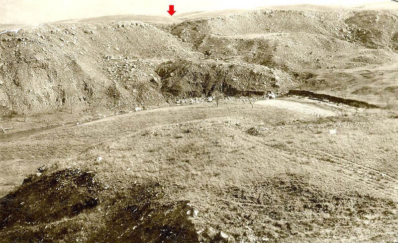 Old photo showing canyon setting with rubble mounds and tire tracks in foreground.