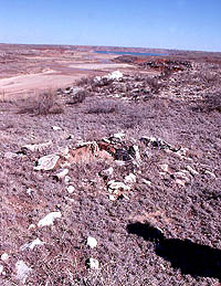 Photo of exposed stone outline of an ancient house. In the background the lake can be seen.