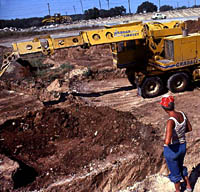 Photo of Jerry Henderson looking on as a Gradall is used to remove Archaic deposits overlying the Paleoindian component. 