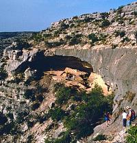 Archeologists carefully make their way across a steep rock slope to join the excavations at Baker Cave, a large occupation shelter located in a side canyon of the Devils River. Photo by Tom Hester.