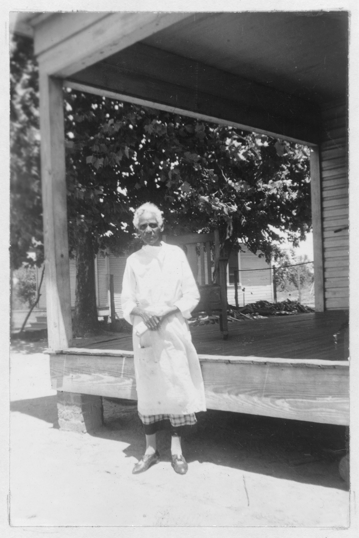 black and white photo of elderly Black woman standing in front of a raised wooden porch