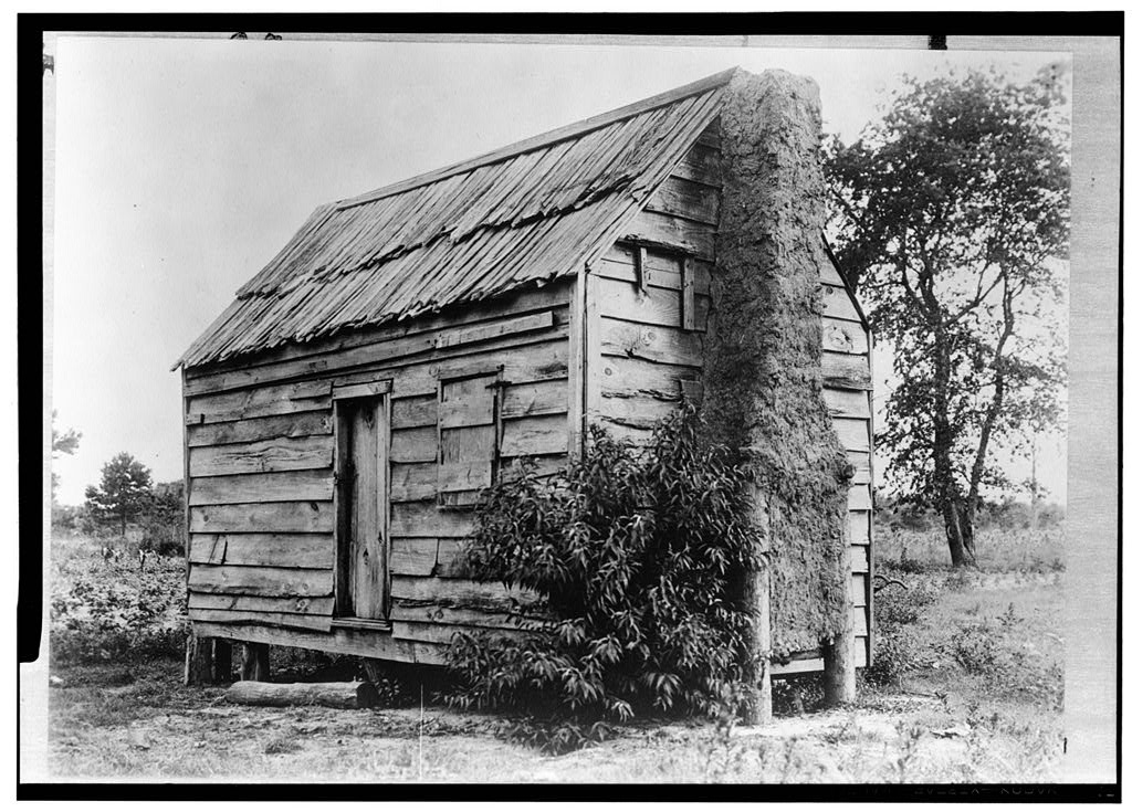 black and white photo of log cabin with large Black family sitting posed