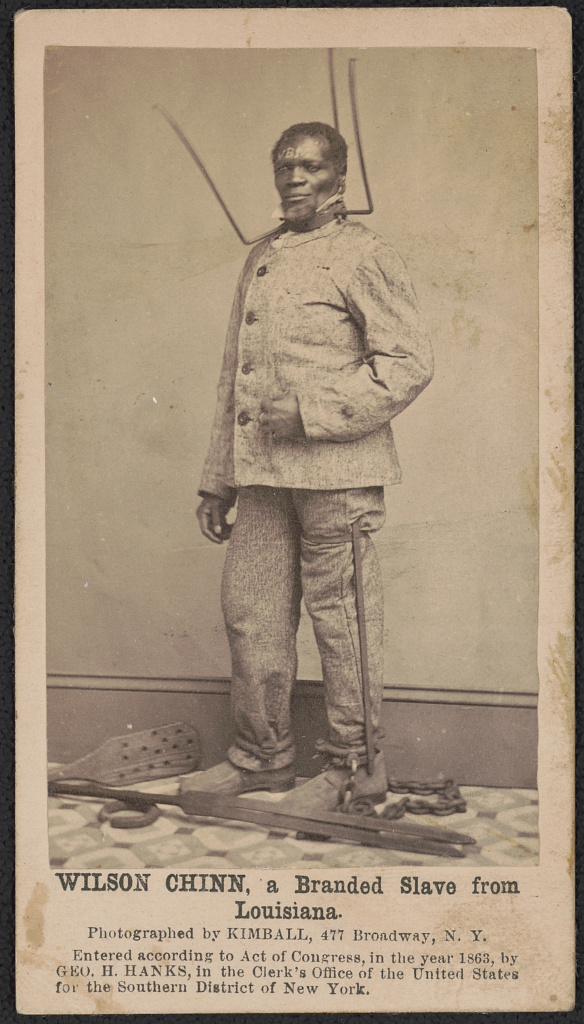 yellowed black and white printed photo of male slave shackled.