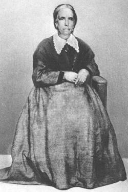 black and white photograph of a older woman seated with her hair pulled back wearing a full-skirted dress